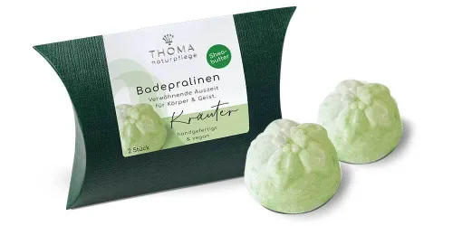 Zwei grüne Badepralinen vor dunkelgrüner Verpackung mit weißer Aufschrift Badepralinen Kraeuter, handgefertigt und vegan von der Naturseifen Manufaktur Uckermark.