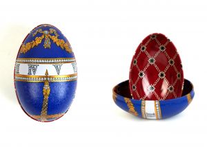 Zwei Metalldosen im Fabergé-Stil, eine geschlossen mit blauem Hintergrund, goldenen Ornamenten und weißem Streifen mit filigranem Muster, die andere geöffnet mit rotem Innenmuster und goldenen Verzierungen, von der Naturseifen Manufaktur Uckermark.