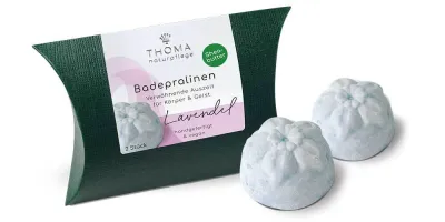 Badepralinen mit Lavendel Zwei hellblaue Badepralinen vor dunkelgrüner Verpackung mit weißer Aufschrift Badepralinen Lavendel, handgefertigt und vegan von der Naturseifen Manufaktur Uckermark.