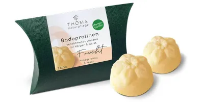 Badepralinen mit Mangobutter- Frucht Zwei gelbliche Badepralinen vor dunkelgrüner Verpackung mit weißer Aufschrift Badepralinen Frucht, handgefertigt und vegan mit Mangobutter von der Naturseifen Manufaktur Uckermark.