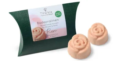 Badepralinen mit Sheabutter - ROSE Zwei rosafarbene Badepralinen in Rosenform vor dunkelgrüner Verpackung mit weißer Aufschrift Badepralinen Rose, handgefertigt und vegan mit Sheabutter von der Naturseifen Manufaktur Uckermark.
