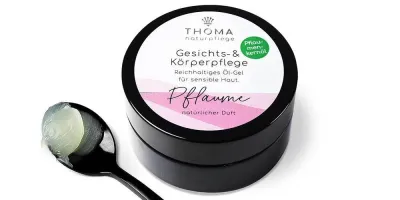 Runde, schwarze Dose mit weiß-rosafarbener Aufschrift Gesichts und Körperpflege Pflaume, reichhaltiges Oel-Gel mit natürlichem Mandelduft für sensible Haut von der Naturseifen Manufaktur Uckermark.