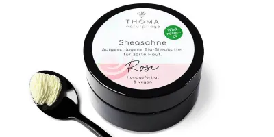 Runde, schwarze Dose mit weiß-rosafarbener Aufschrift Sheasahne Rose, aufgeschlagene Bio-Sheabutter mit Wildrosenoel, handgefertigt und vegan von der Naturseifen Manufaktur Uckermark.
