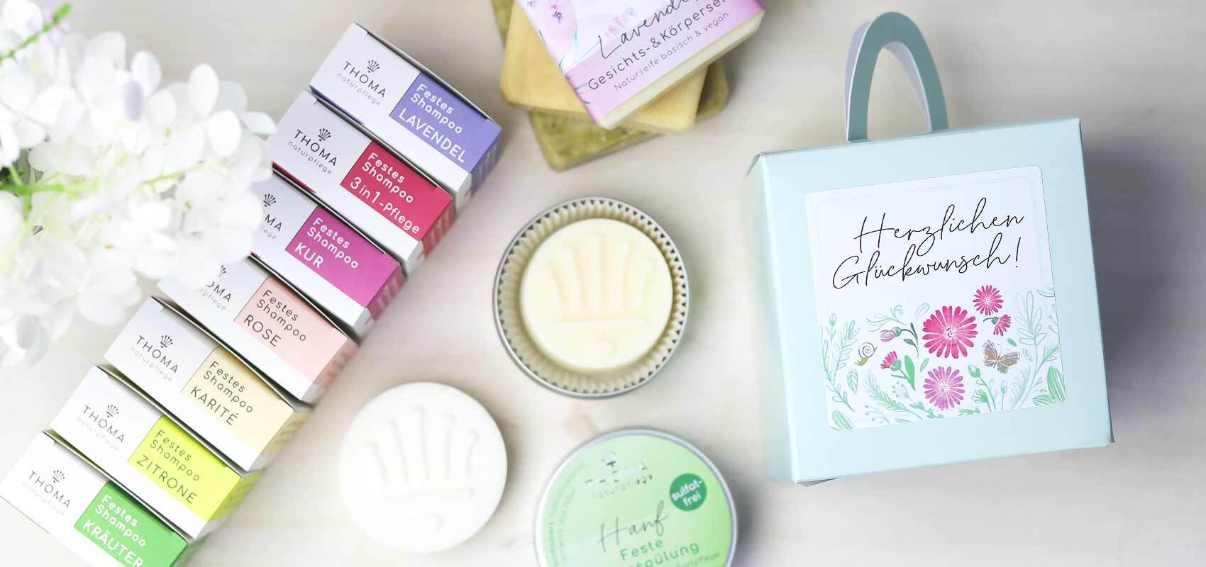 Eine Auswahl an festen Shampoos von Thoma Naturpflege in verschiedenen Sorten wie Lavendel, Karité und Zitrone. Im Bild sind außerdem handgemachte Seifen und eine Geschenkbox mit der Aufschrift 